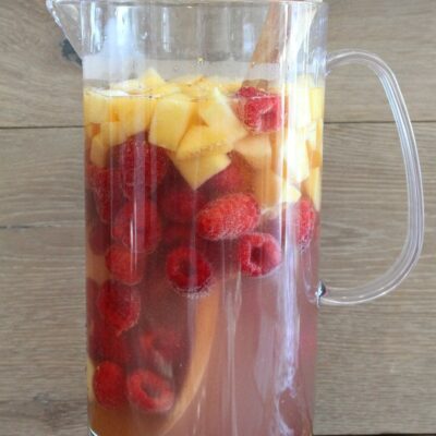 pitcher of peach and raspberry sangria with a wood backdrop