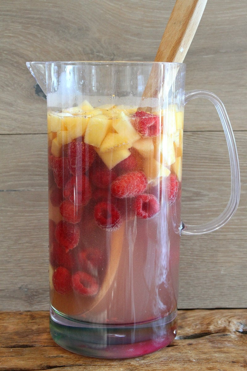 pitcher of peach and raspberry sangria with a wood backdrop