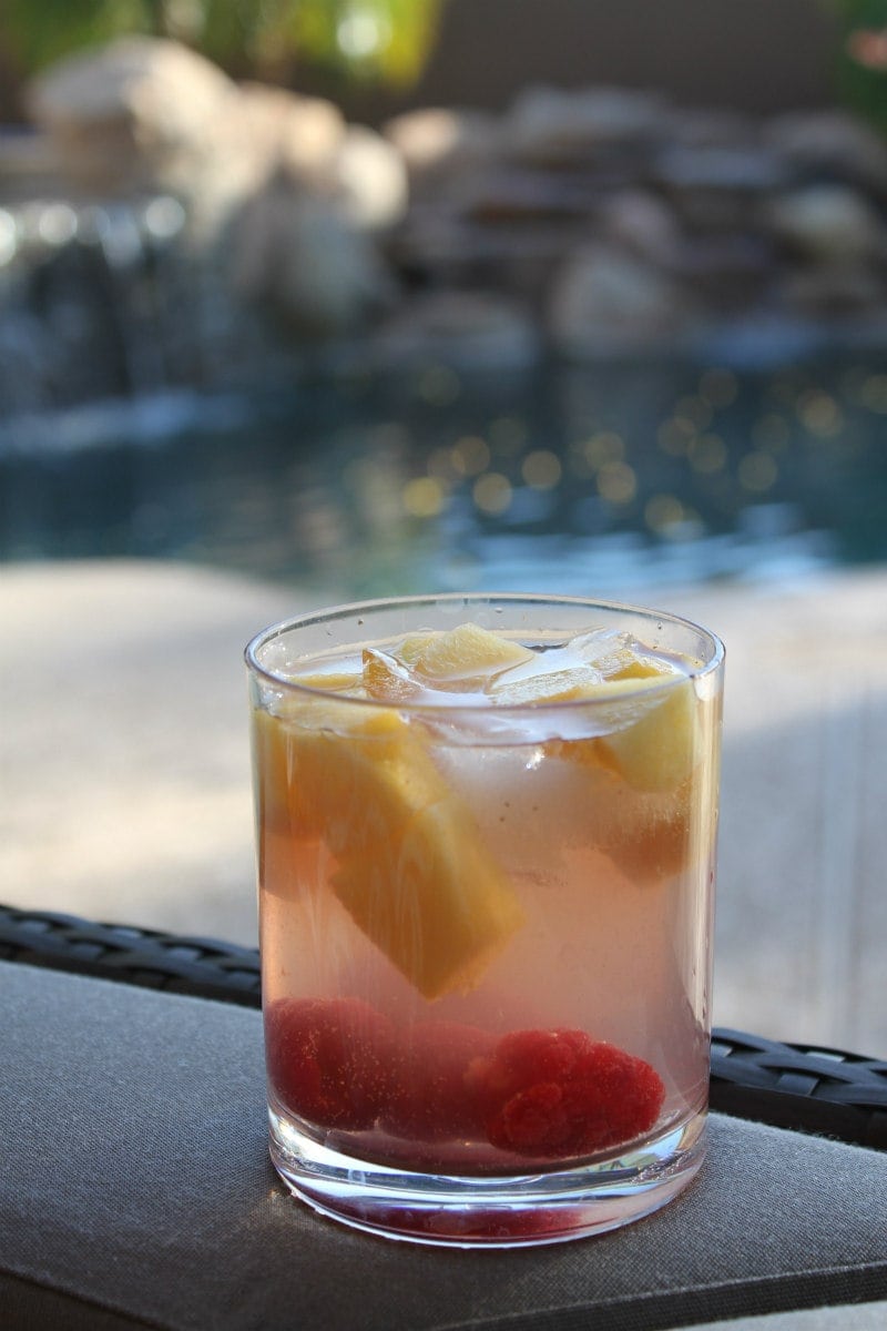 peach and raspberry sangria in a glass with a backyard backdrop