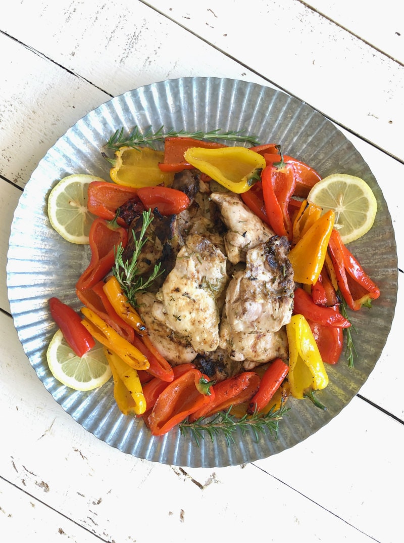 lemon oregano grilled chicken thighs in the center of a metal platter surrounded by grilled peppers and lemon slices