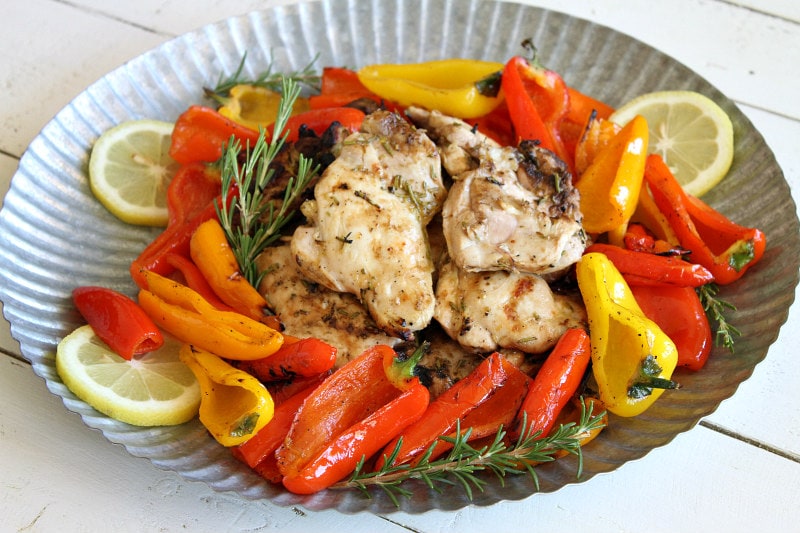 lemon oregano grilled chicken thighs in the center of a metal platter surrounded by grilled peppers