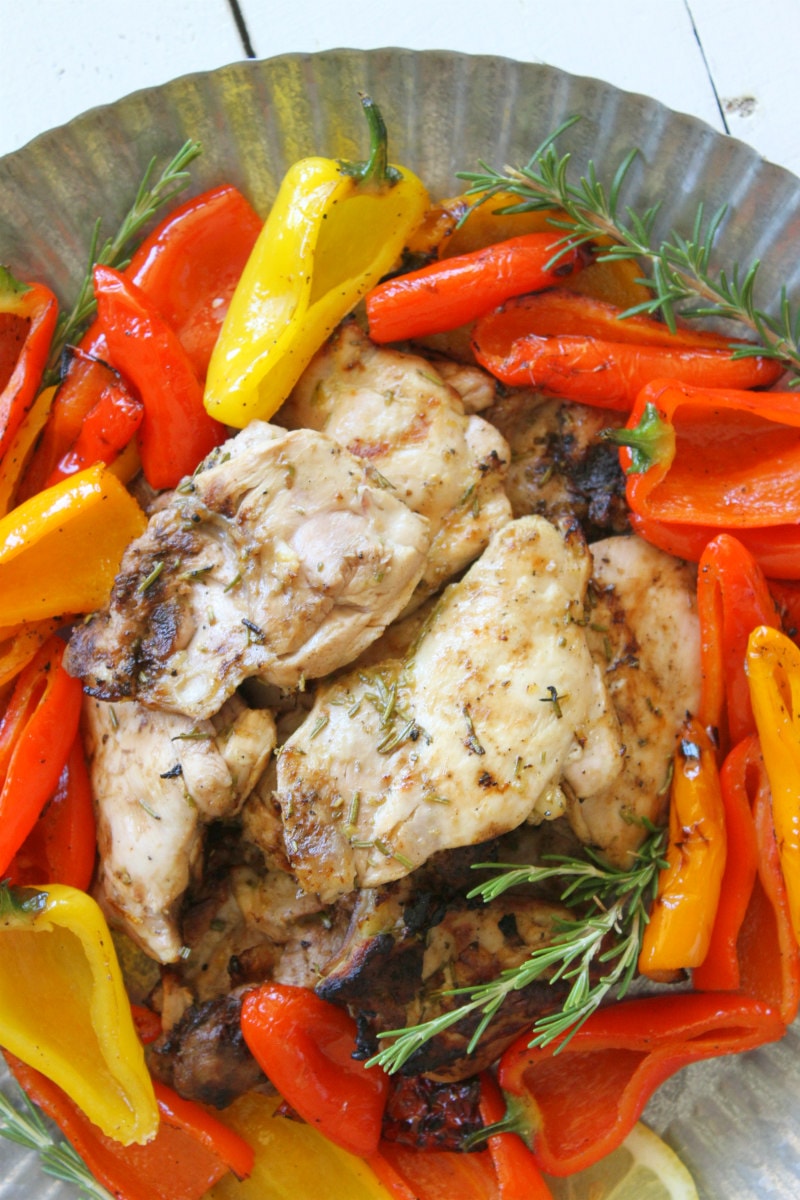 lemon rosemary grilled chicken thighs in the center of a metal platter surrounded by grilled peppers