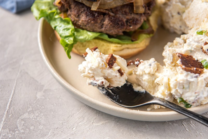 a forkful of potato salad on a white plate served with a burger