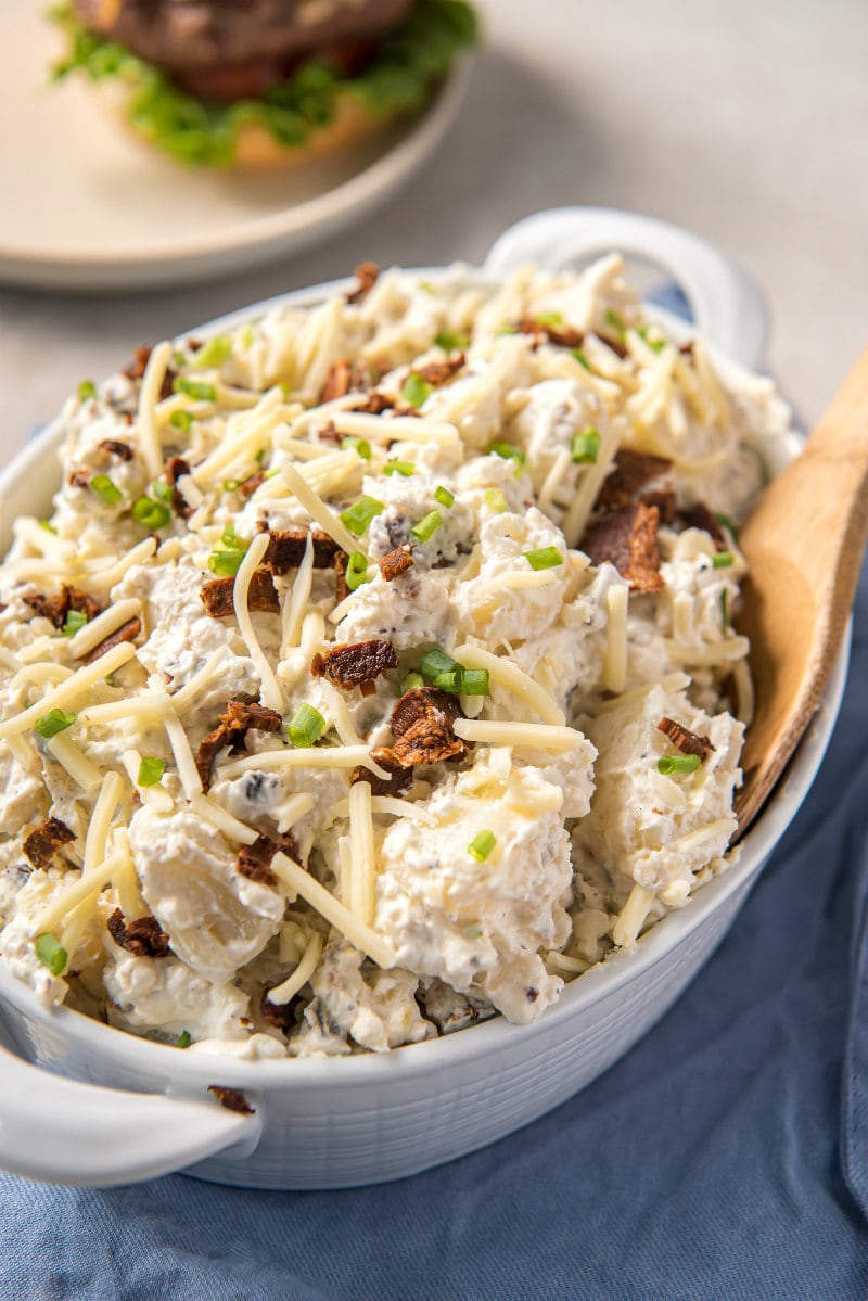 loaded baked potato salad in a white dish with a wooden spoon