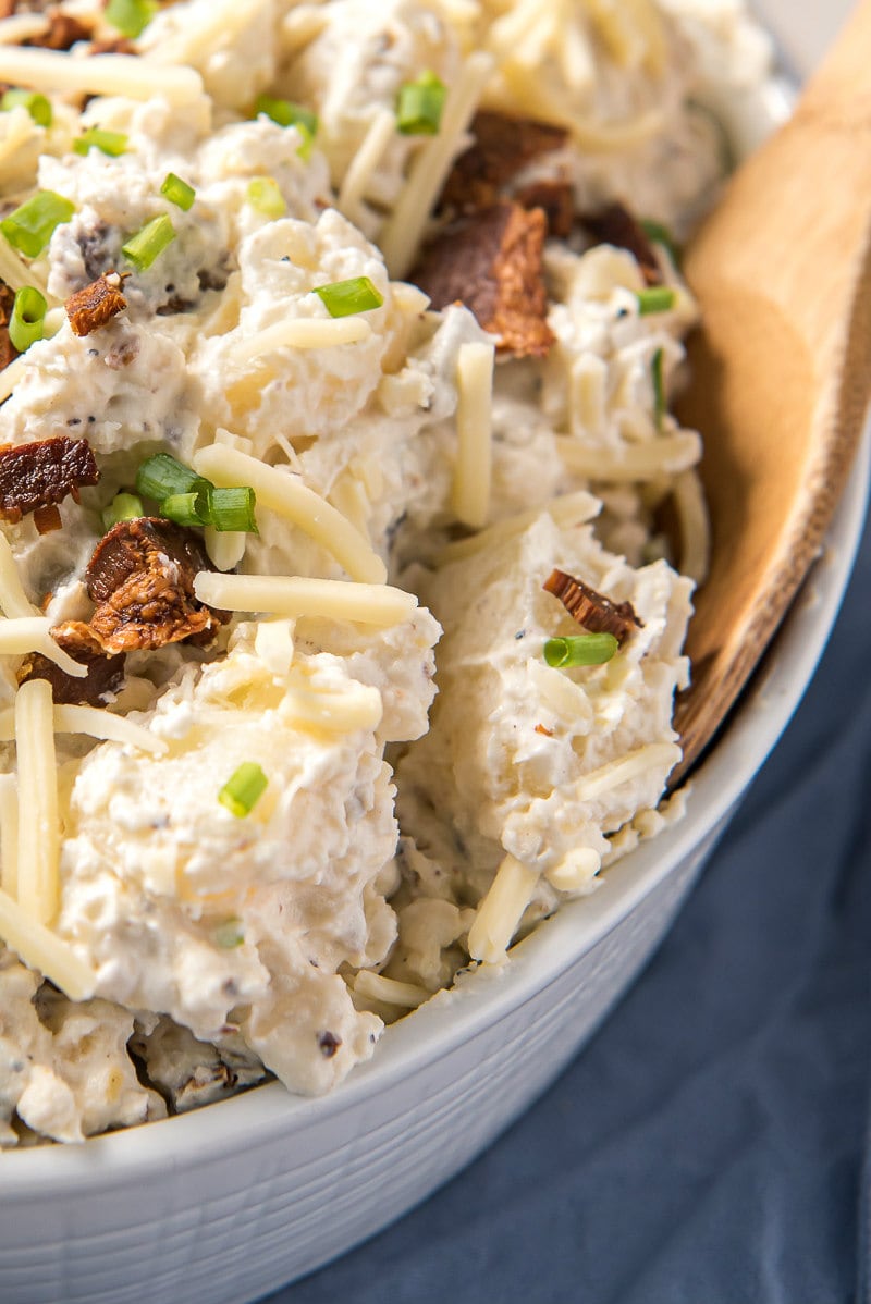 loaded baked potato salad in a white dish with a wooden spoon