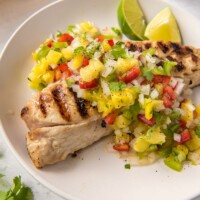 overhead shot of red snapper with pineapple salsa on a white plate with lime garnish