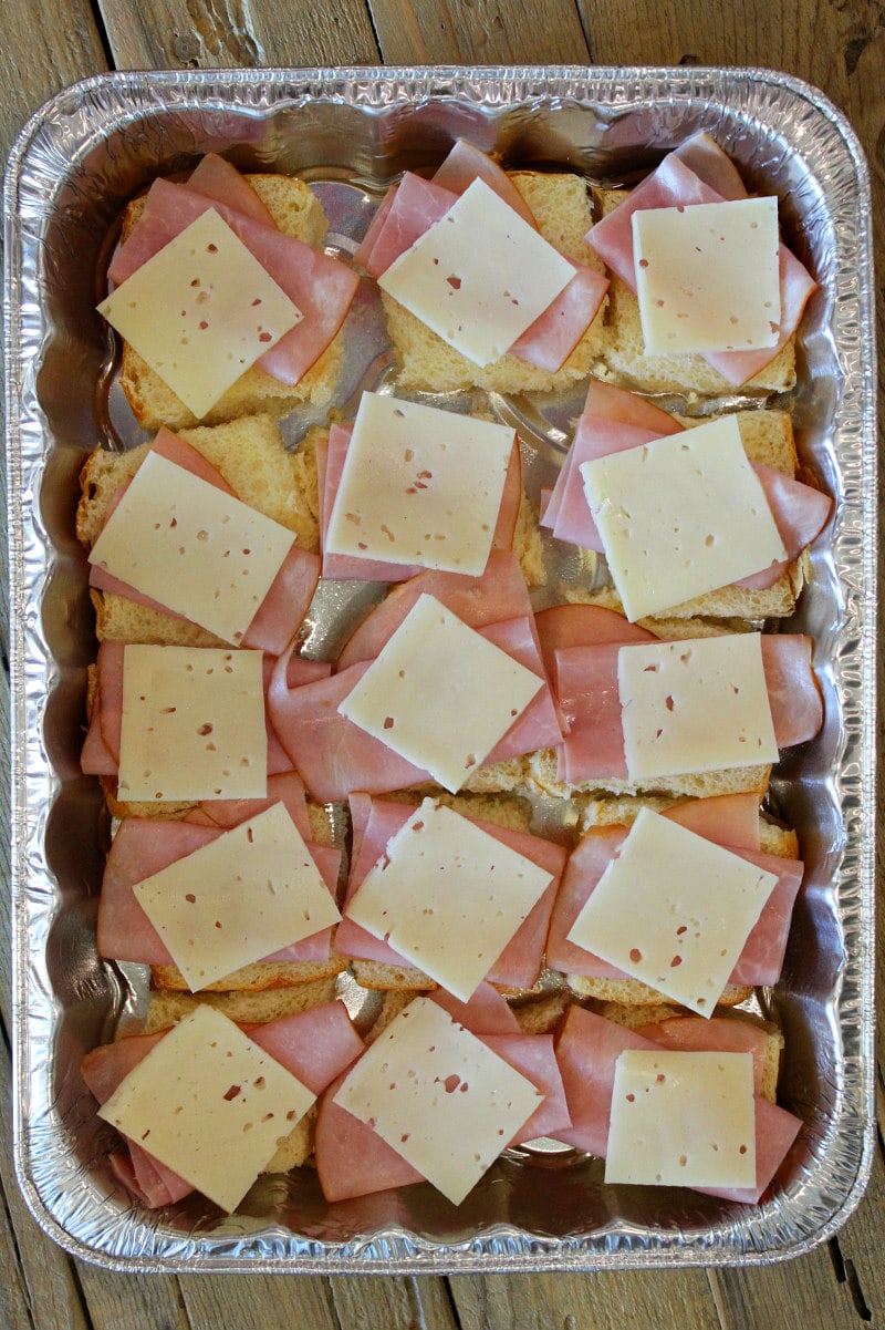 overhead shot of process of making pan of cuban sliders with layers of ham and cheese