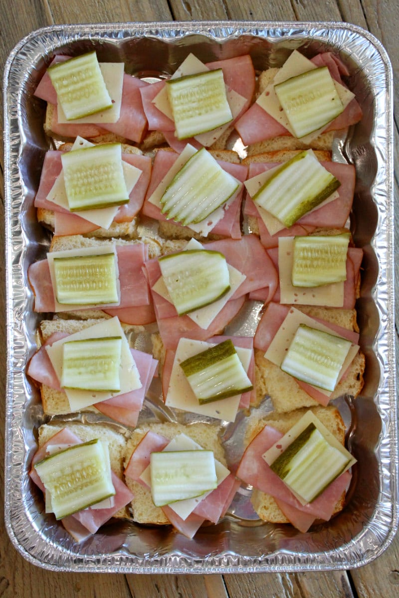 overhead shot of a pan of cuban sliders in the making process- layering ham, cheese and pickle