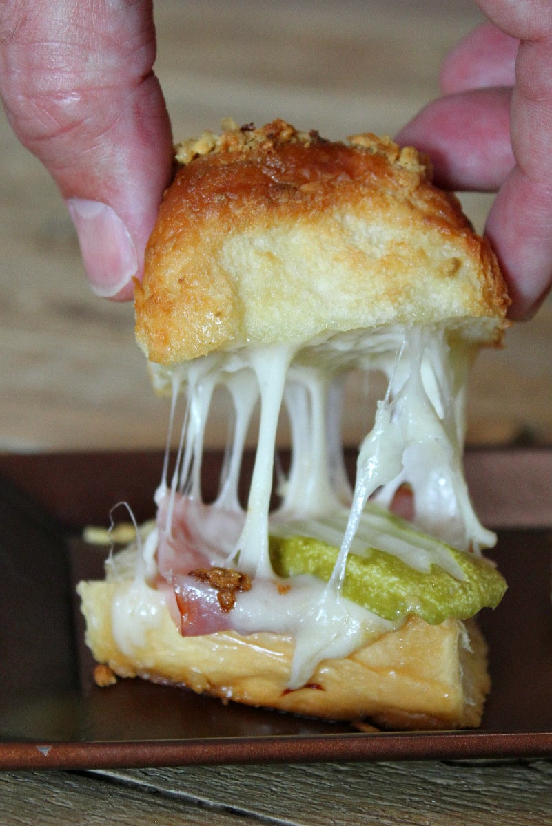 hand pulling a baked cuban slider apart to show gooey melted cheese