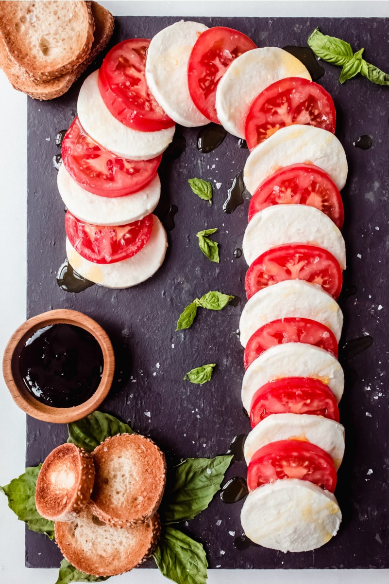 Candy Cane Caprese Board on a black board with balsamic glaze and sliced bread