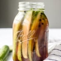 side shot of beer pickles in a tall jar with a blue and white napkin on the side