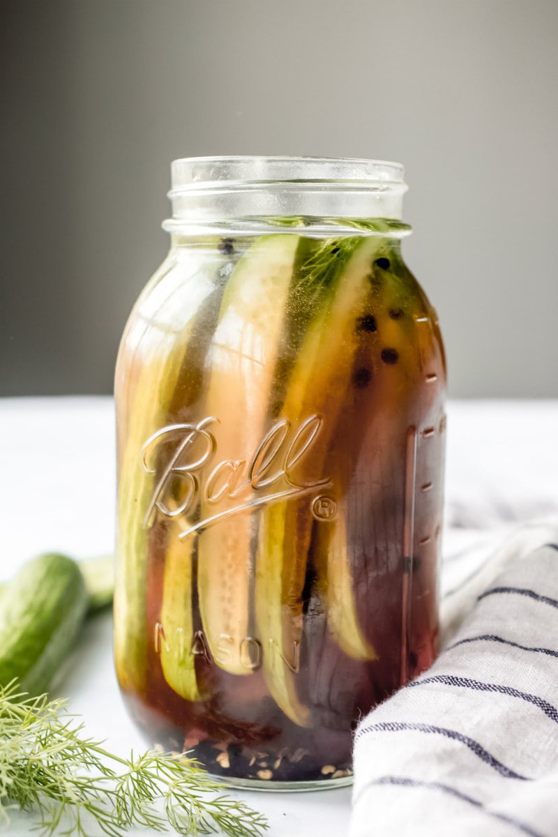 side shot of beer pickles in a tall jar with a blue and white napkin on the side