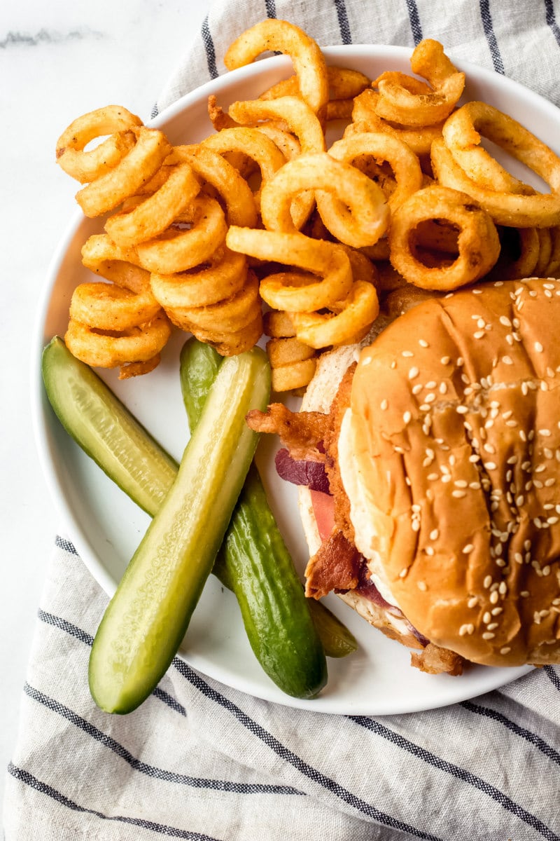 overhead shot of pickles served with curly fries and a burger served on a white plate