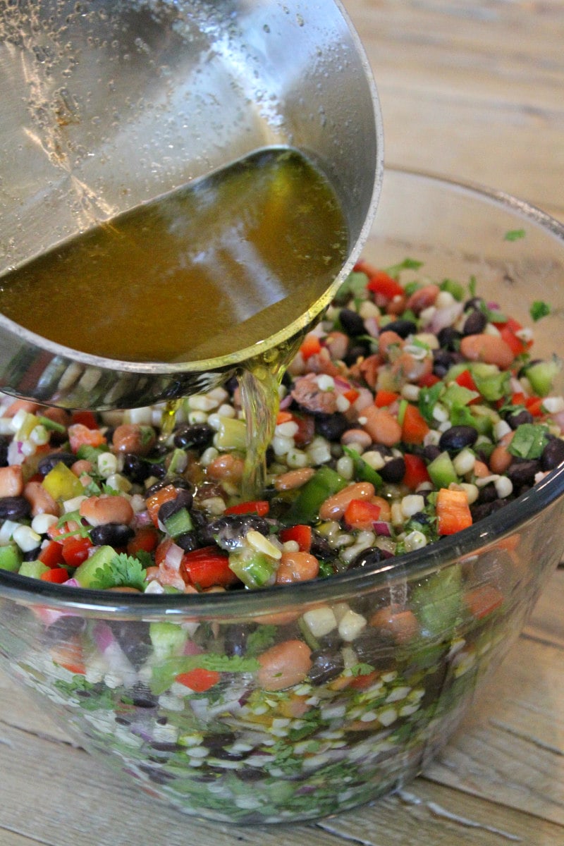 pouring dressing onto texas caviar in a glass bowl