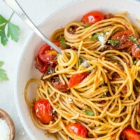 spaghetti with three tomato sauce in a white bowl with a serving spoon