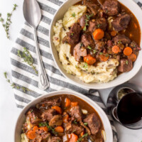 overhead shot of two servings of beef bourguignon displayed on a blue and white striped napkin with a spoon