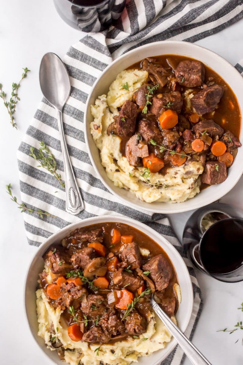 overhead shot of two servings of beef bourguignon displayed on a blue and white striped napkin with a spoon