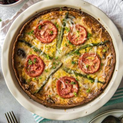 Overhead shot of Garden Vegetable Quiche on a white napkin with forks and fresh fruit in a bowl