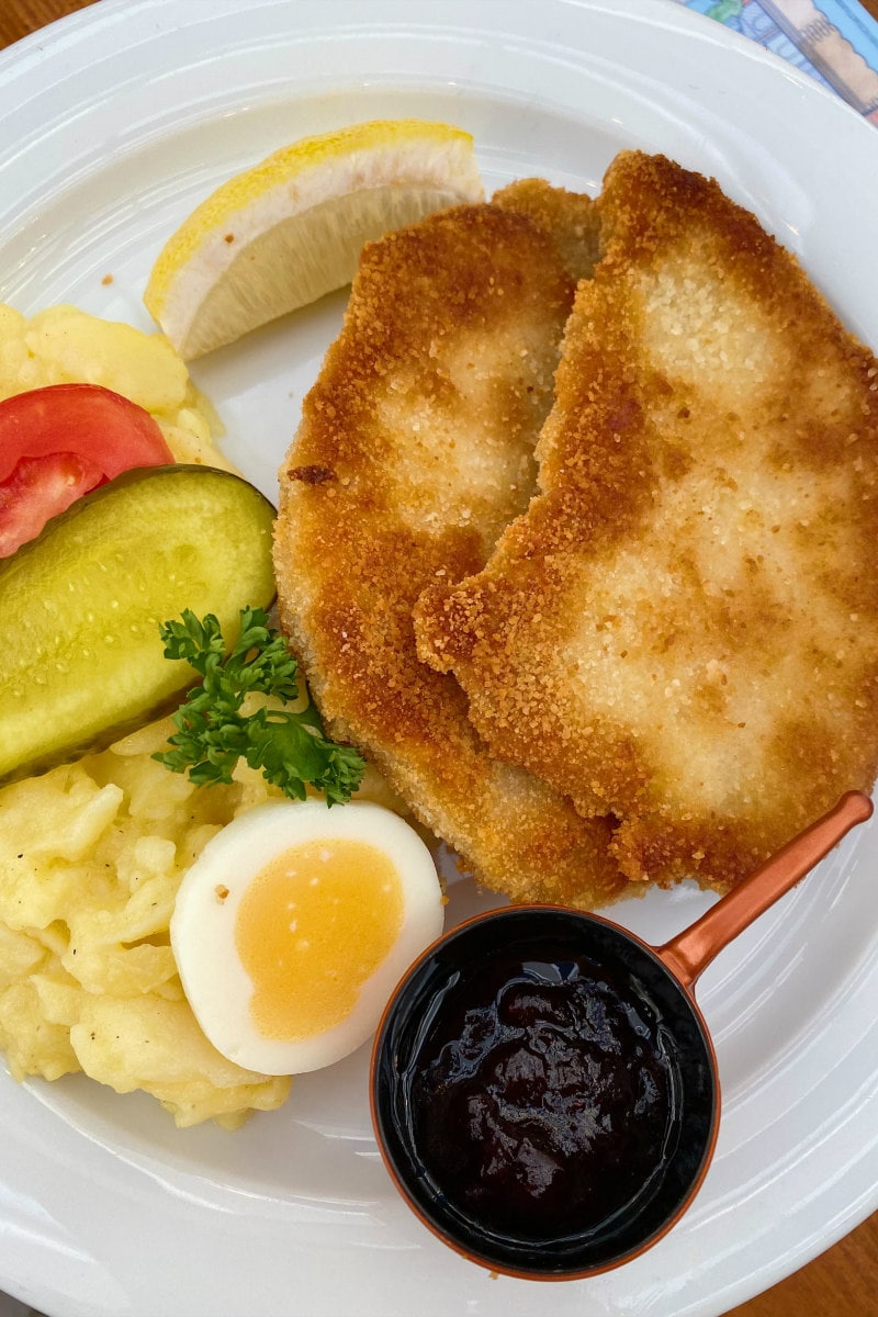 Schnitzel, potato salad, egg and pickle on a white plate