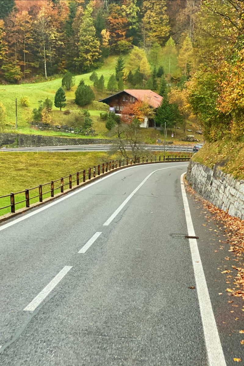 Driving in the Swiss Alps along a highway. Green countryside in view with trees and a house.