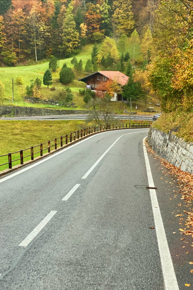 Driving in the Swiss Alps along a highway. Green countryside in view with trees and a house.