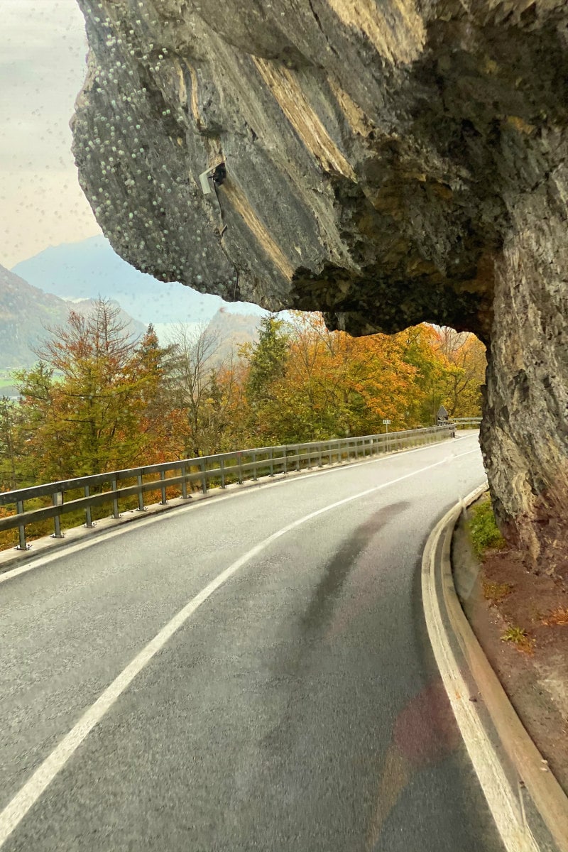 View of the highway to the Swiss Alps with large rock formation hanging over the road