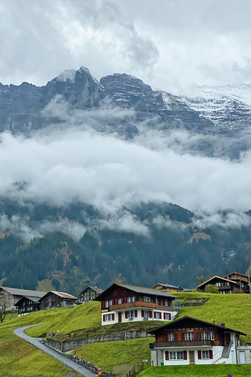 Green Valley with houses below the clouded Swiss Alps 