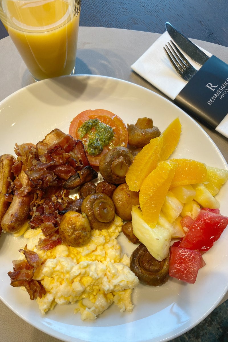 plate of breakfast- eggs, fruit and sausages on a white plate with place setting and orange juice