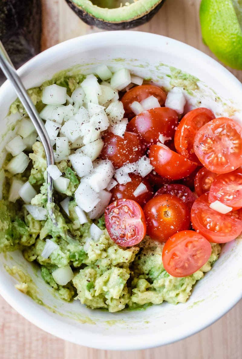 making filling for stuffed avocados (onion, avocado, tomato in a white bowl)