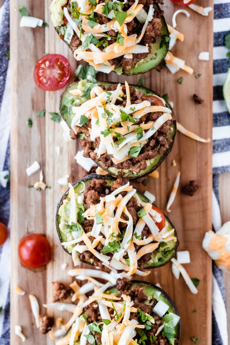 four avocado halves stuffed with taco filling on a wooden cutting board