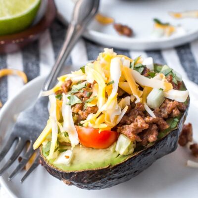 half an avocado stuffed with taco filling. On a white plate with a fork.