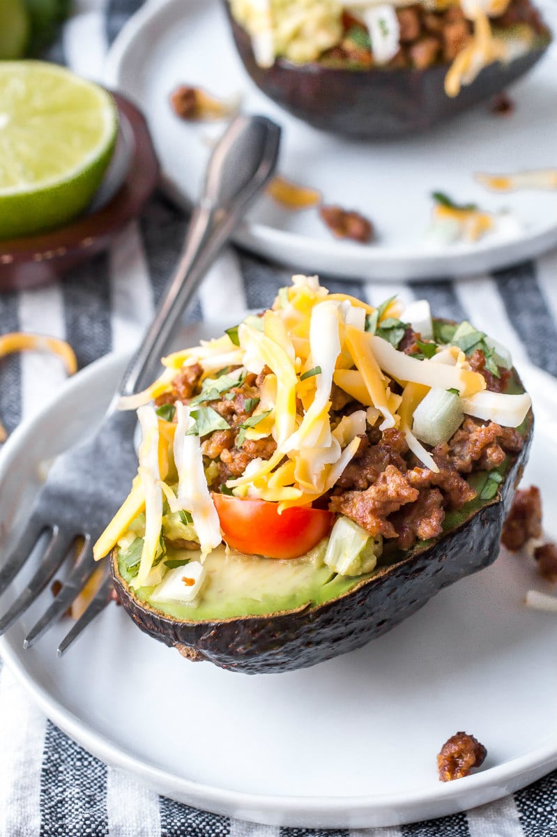 half an avocado stuffed with taco filling. On a white plate with a fork.