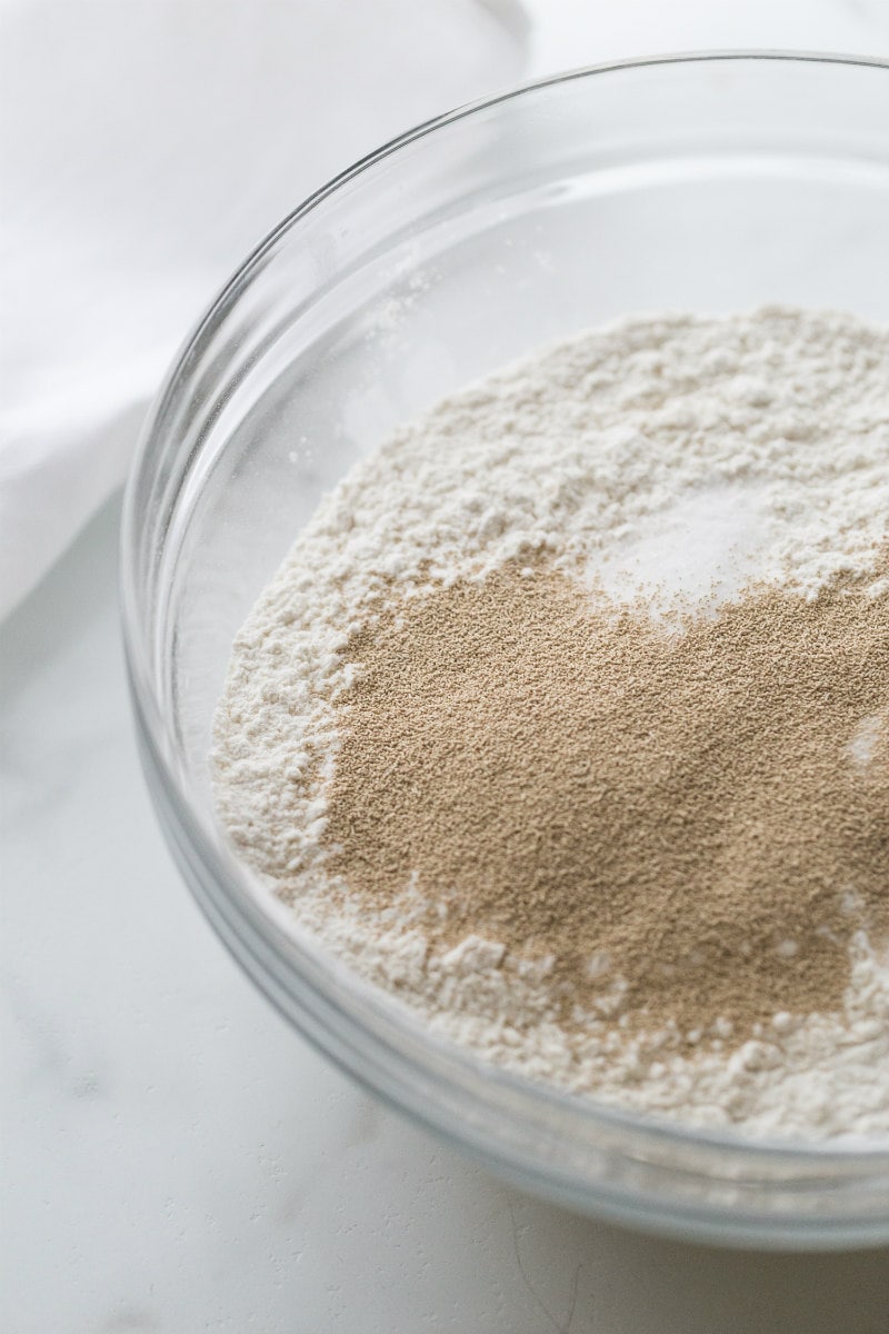 Flour and yeast for English Muffin Bread in a glass bowl on a marble counter