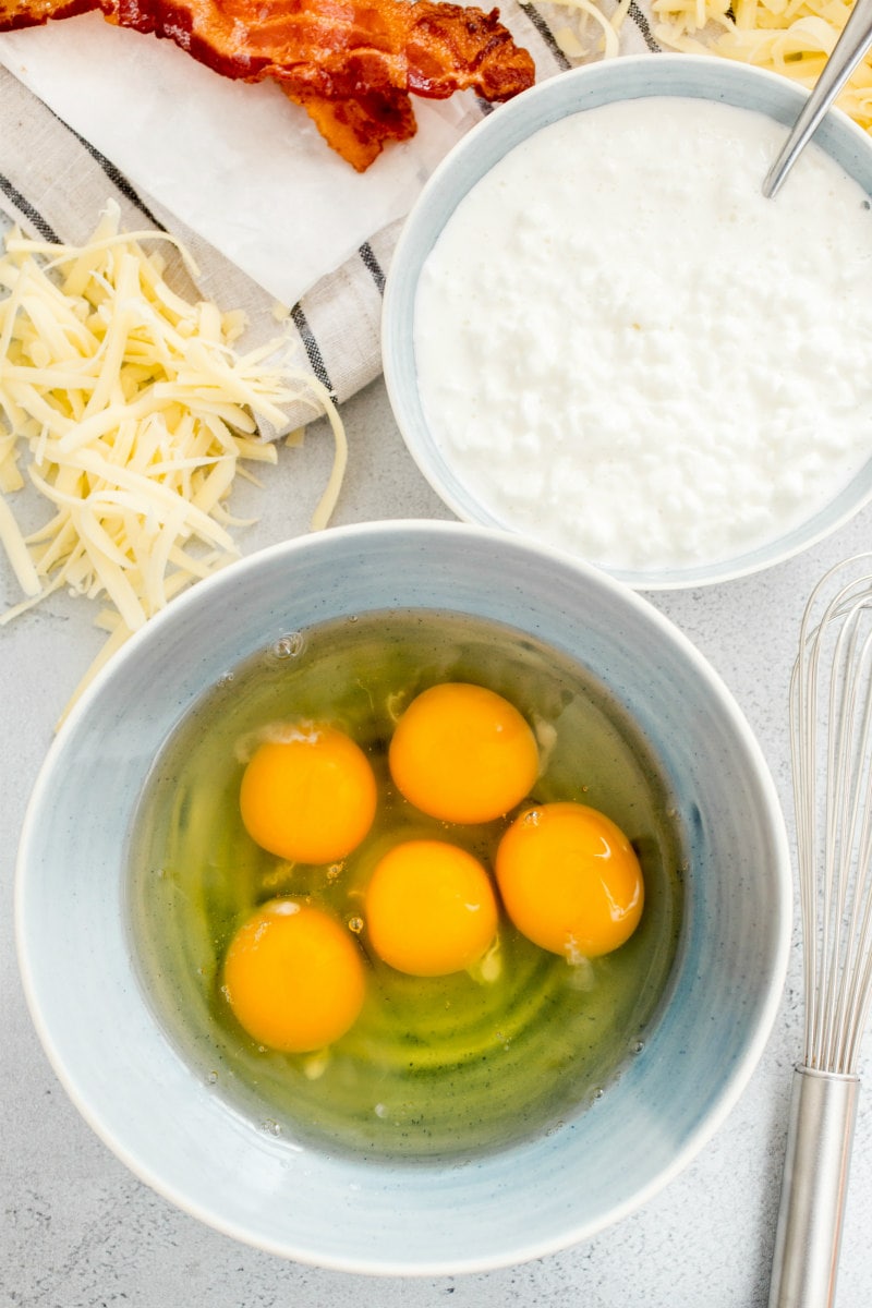 an overhead shot of the ingredients needed for copycat starbucks egg bites: bacon, cheese, cottage cheese and eggs