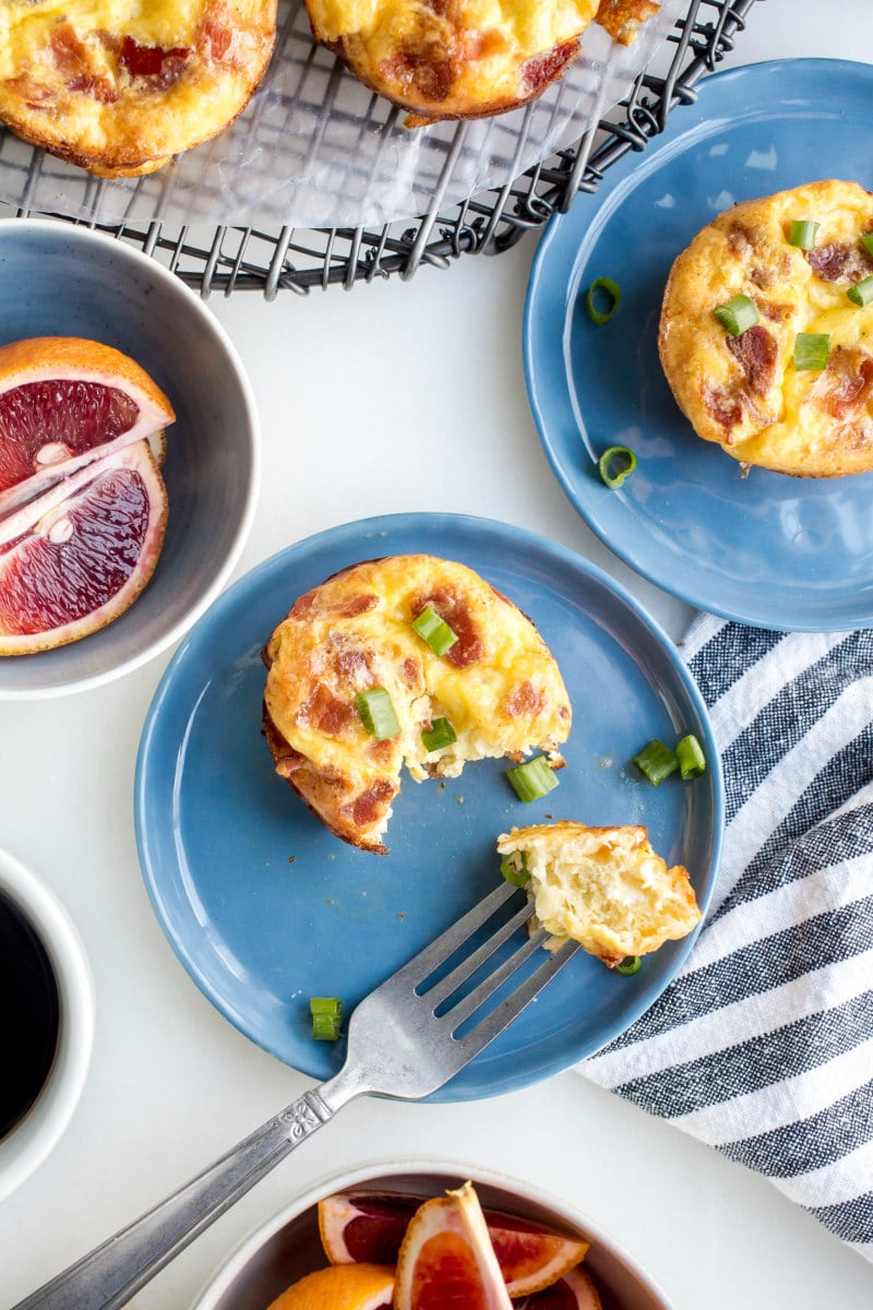 Copycat Starbucks Egg Bites recipe from RecipeGirl.com : Bacon and Gruyere Egg Bites overhead shot of using a fork to eat copycat starbucks egg bites on a blue plate with a striped napkin