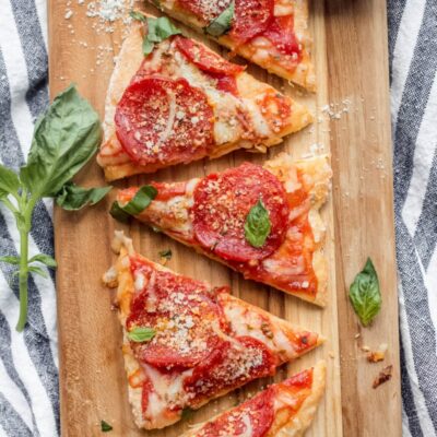 sliced pepperoni pizza on a cutting board garnished with fresh basil set on a white and blue striped napkin