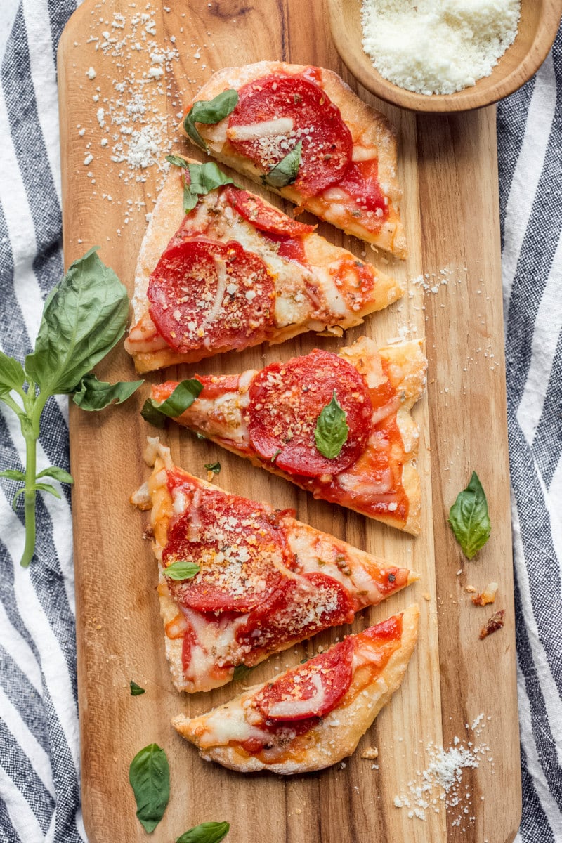 sliced pepperoni pizza on a cutting board garnished with fresh basil set on a white and blue striped napkin