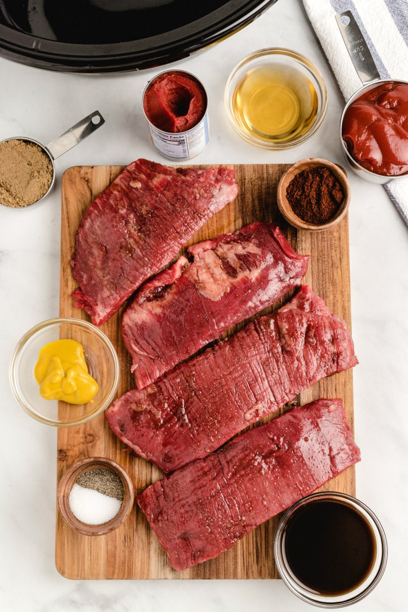 ingredients displayed for making barbecue beef sandwiches- steak cut into slices and condiments for sauce