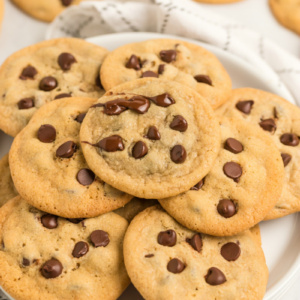 chocolate chip cookies displayed on a white platter on top of a white and gray plaid napkin