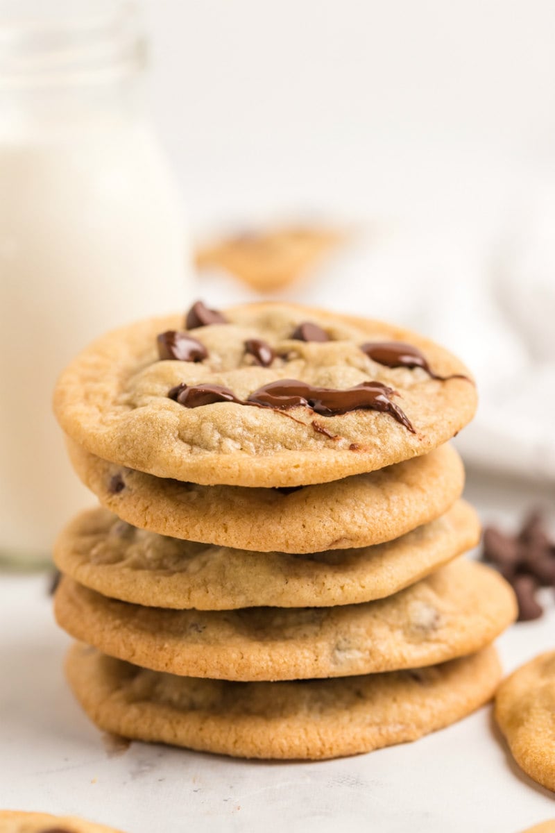 stack of chocolate chip cookies with a glass of milk in the background