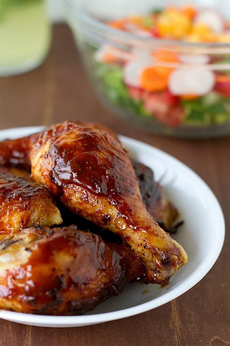 Oven Baked BBQ Chicken on a white plate with salad displayed in the background