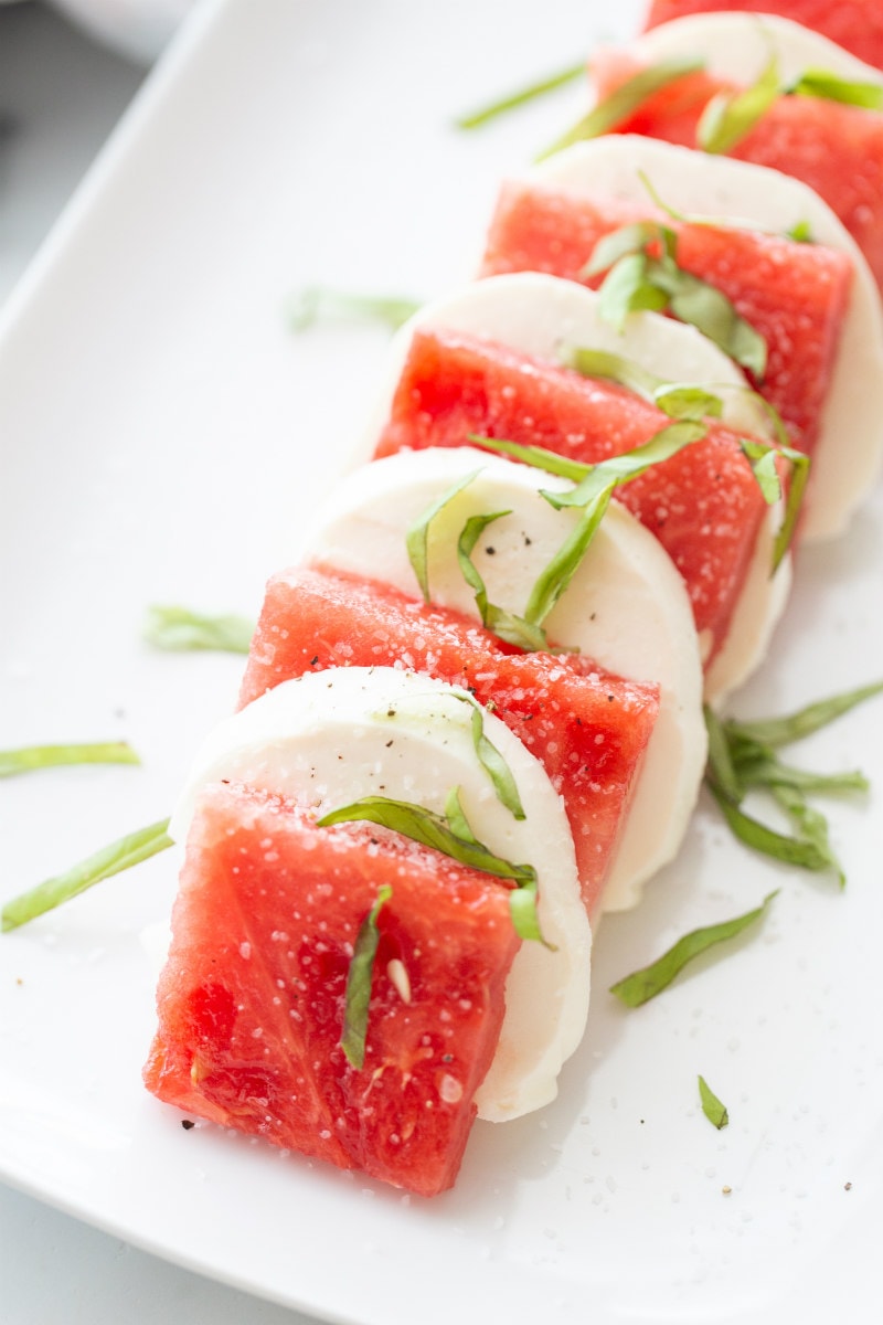 watermelon caprese salad on a white plate waiting to be topped with balsamic glaze