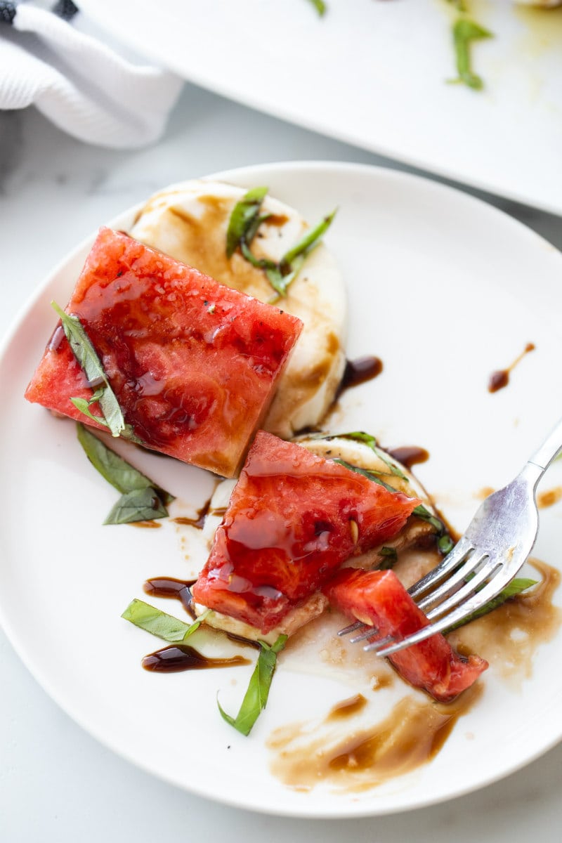 watermelon caprese salad on a white plate being eaten with a fork
