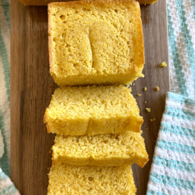 overhead shot of buttermilk cornbread sliced on a cutting board set on a white/teal striped cloth napkin