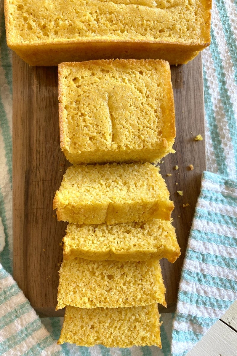 overhead shot of buttermilk cornbread sliced on a cutting board set on a white/teal striped cloth napkin