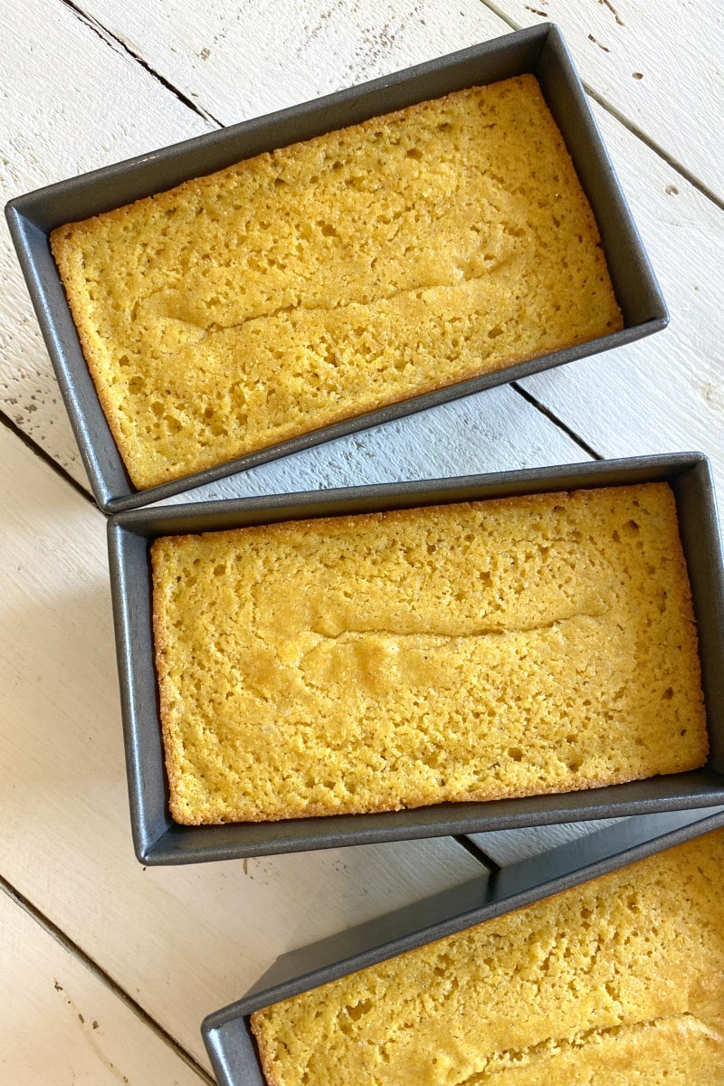 overhead shot of three mini loaf pans with buttermilk cornbread in them. set on a white wood board