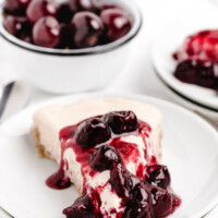 slice of cherries jubilee ice cream pie on a white plate with a bowl of fresh cherries in the background