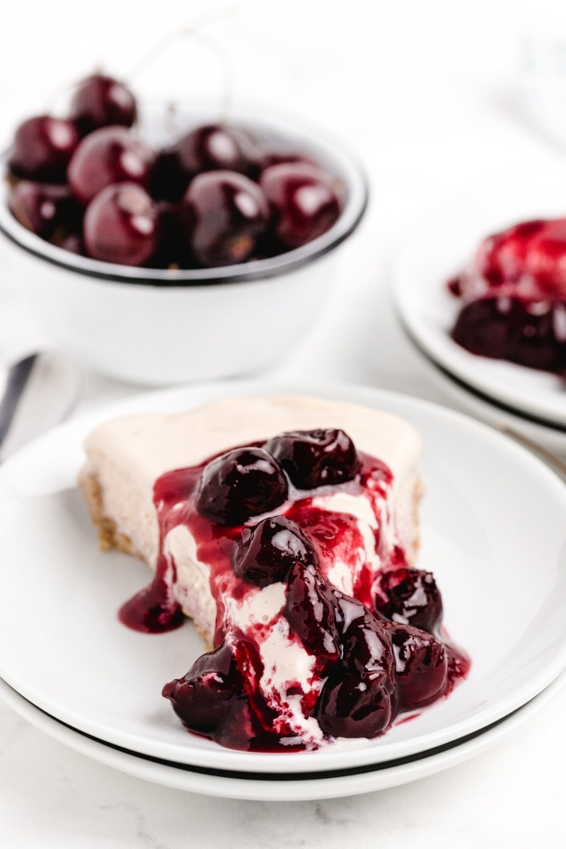 slice of cherries jubilee ice cream pie on a white plate with a bowl of fresh cherries in the background