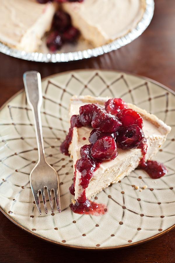 slice of cherries jubilee ice cream pie on an off white patterned plate with a fork and a peek at the pie in the background