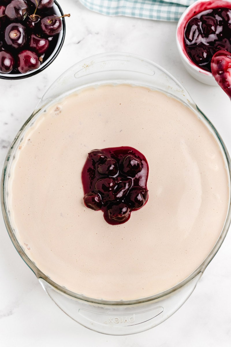 Cherries Jubilee Ice Cream Pie in a pyrex pie pan with cherry sauce on top with bowls of cherry sauce in the background